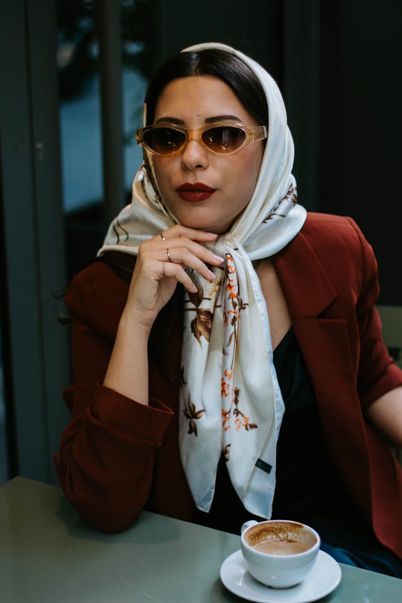 Stylish woman wearing a hijab and sunglasses enjoys coffee in Istanbul café.