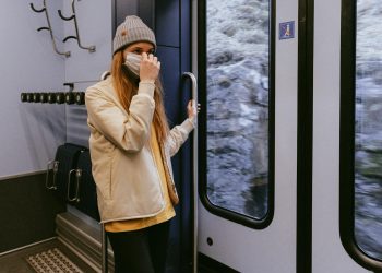 Woman in Beige Coat and Black Pants Standing Beside Glass Window