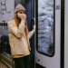 Woman in Beige Coat and Black Pants Standing Beside Glass Window