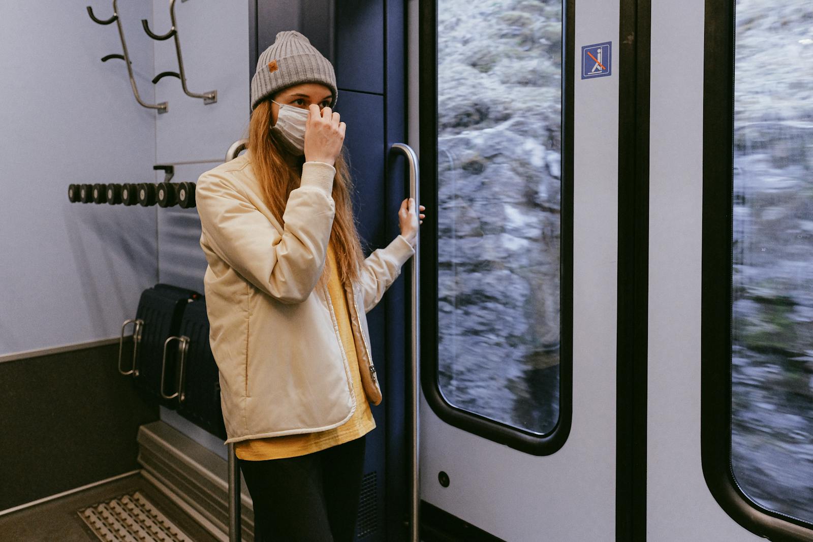 Woman in Beige Coat and Black Pants Standing Beside Glass Window