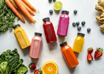 Colorful Bottles with Smoothies Beside Carrots, Ginger, Leaves and Berries