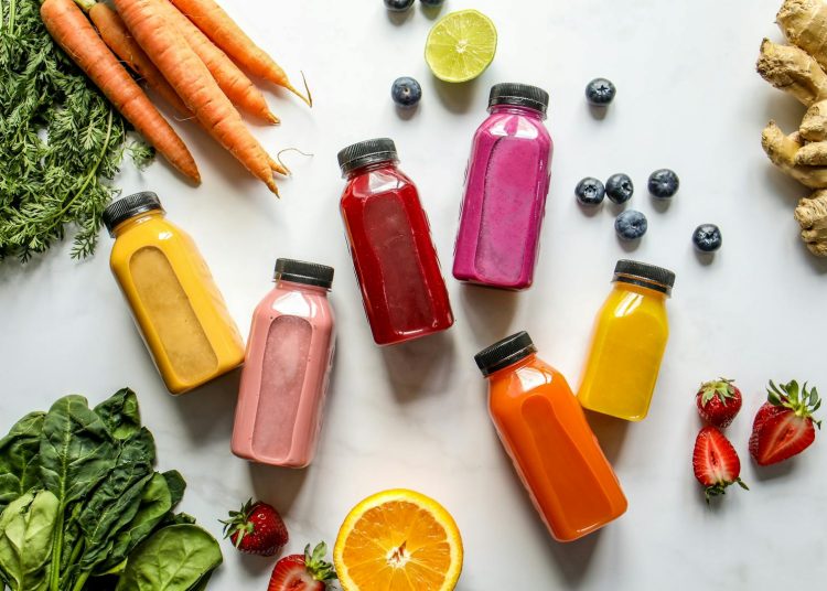 Colorful Bottles with Smoothies Beside Carrots, Ginger, Leaves and Berries