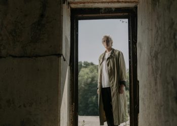Senior Man in White Shirt and Beige Trench Coat Standing on a Doorway