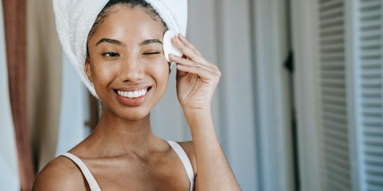 Smiling ethnic woman wiping face skin in morning