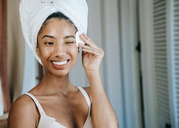 Smiling ethnic woman wiping face skin in morning