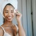 Smiling ethnic woman wiping face skin in morning