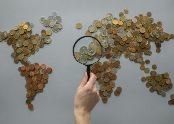 Anonymous person with magnifying glass over world map of coins
