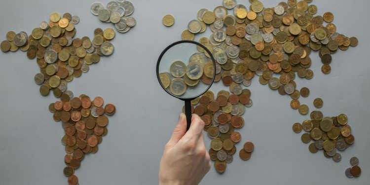 Anonymous person with magnifying glass over world map of coins