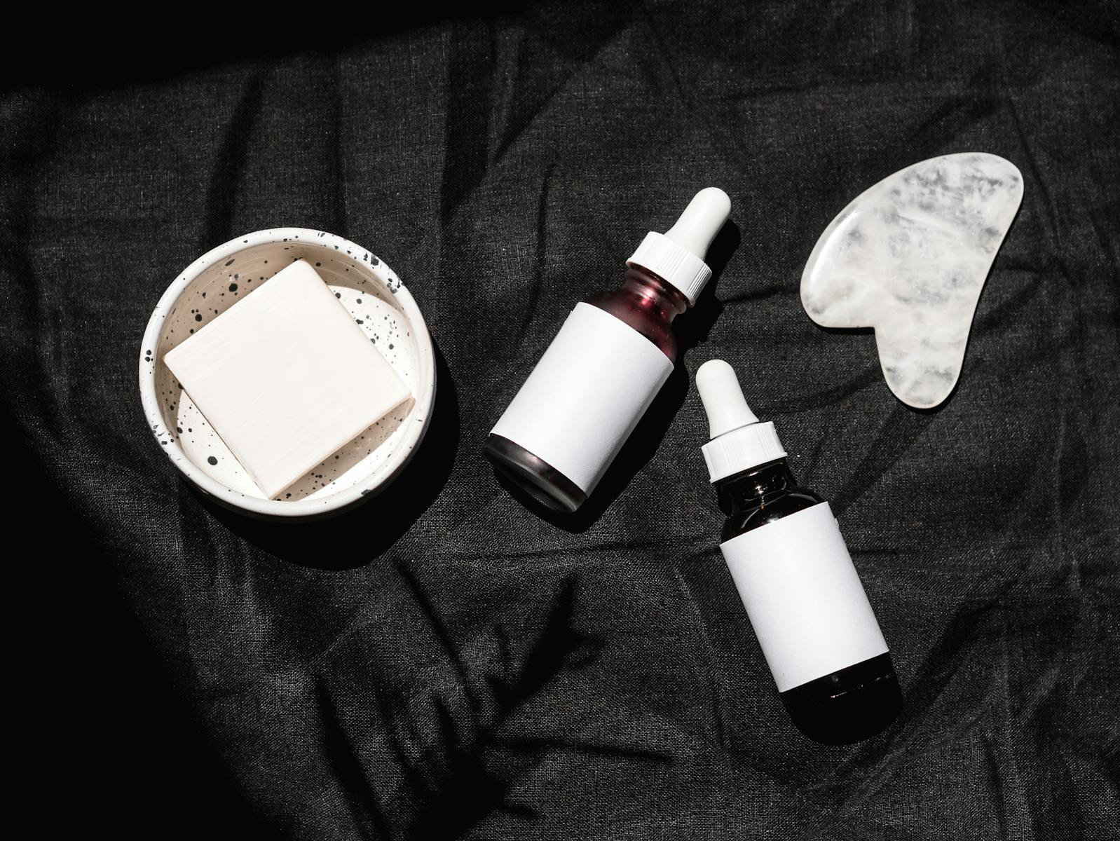 Brown Glass Bottles on Black Textile Beside Gua Sha and Soap