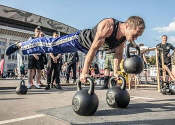 Man in Black Tank Top Doing Push Ups with Kettlebell on Mouth