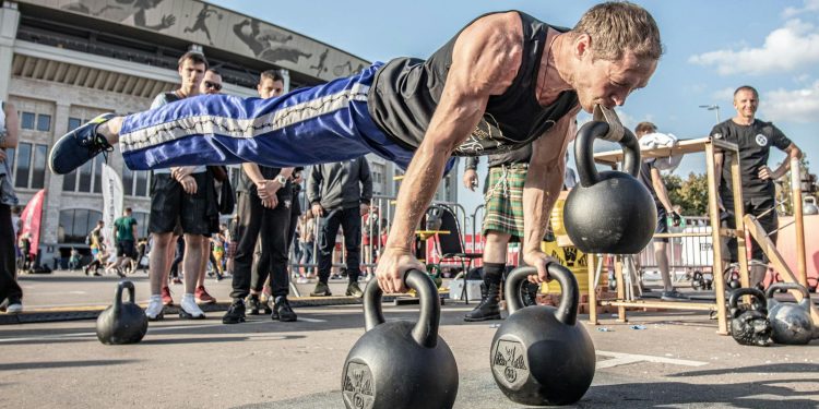 Man in Black Tank Top Doing Push Ups with Kettlebell on Mouth
